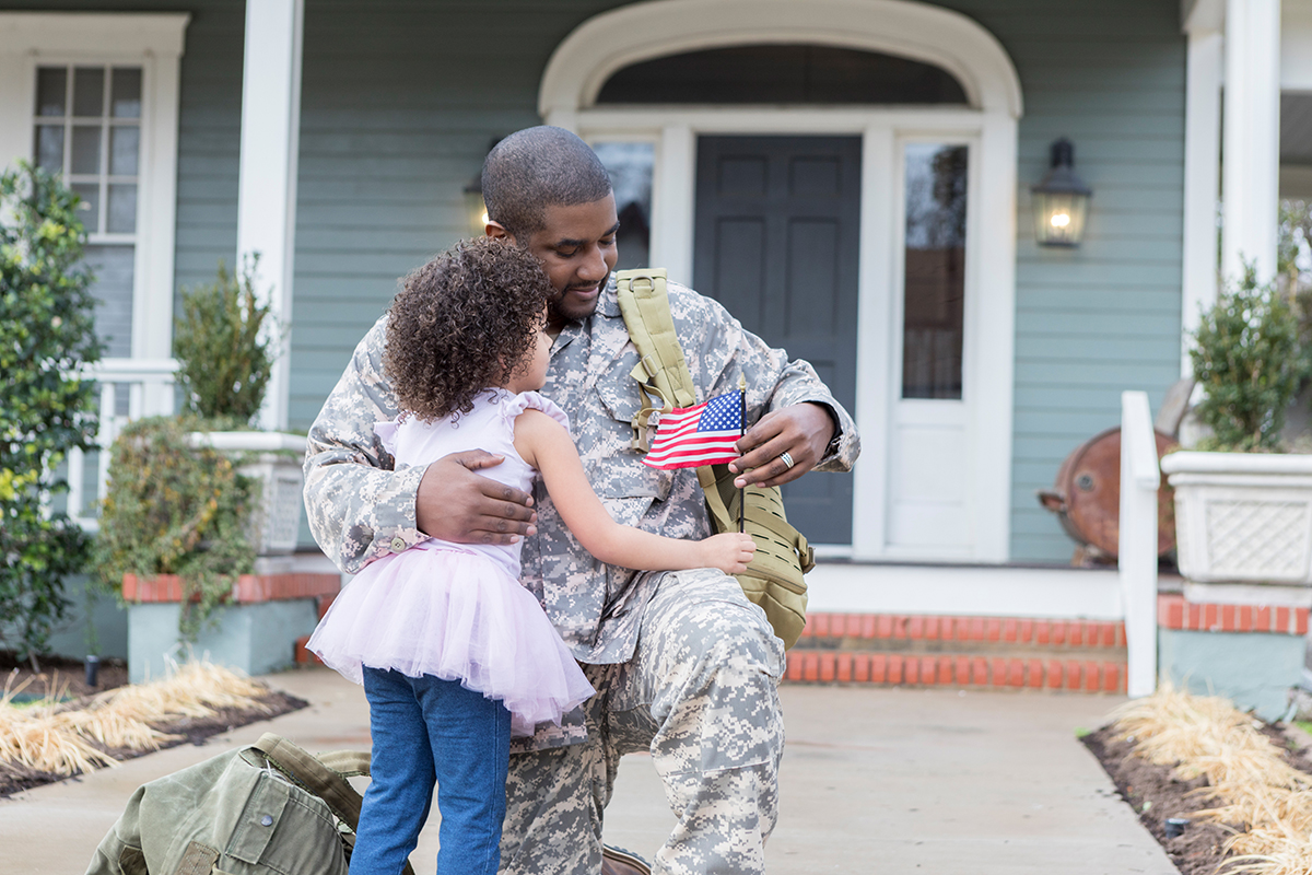 Male veteran embracing his young daughter in front of their home