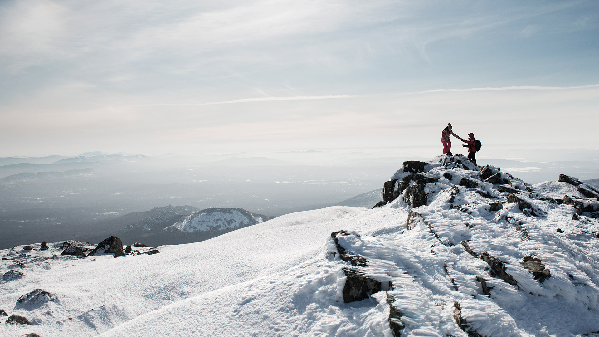 Hiker lending a helping hand to another hiker climbing a summit in the snow