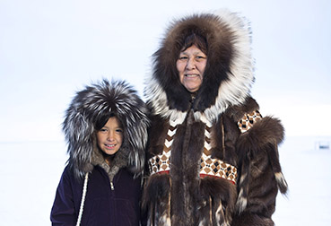 Female Inupiaq elder and young girl looking at camera while wearing traditional alaska native parkas